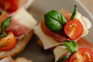 Close-up of toasted bruschetta slices topped with prosciutto, mozzarella cheese, cherry tomatoes, and fresh basil.
