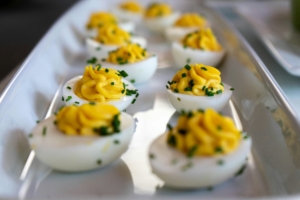 A white platter featuring deviled eggs with piped yellow filling and chive garnish