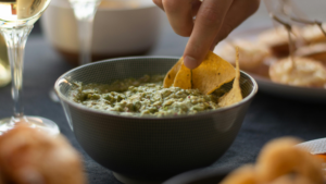 A hand dipping a tortilla chip into a bowl of creamy spinach and artichoke dip.