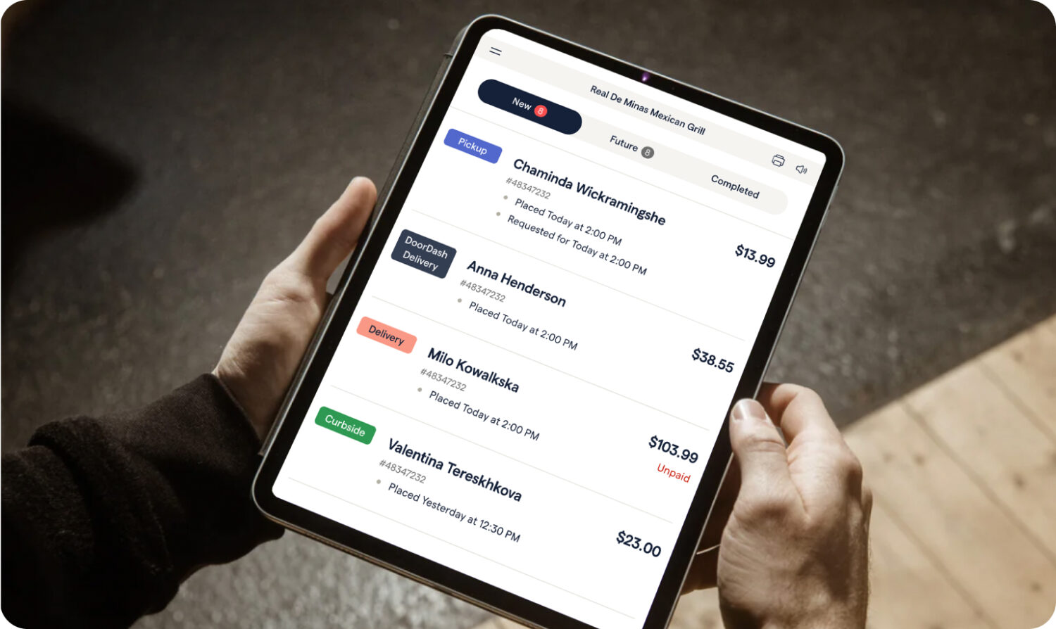 A person holds a tablet. On screen is their business manager app provided by ChowNow