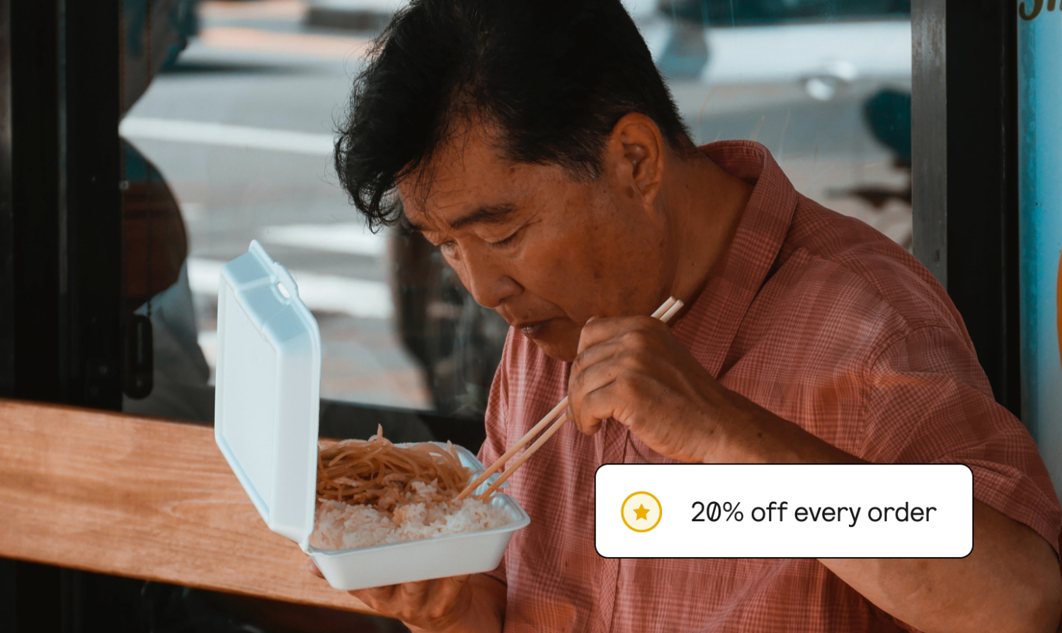 A person is eating from a takeout container. In the corner, it's implied that he saved 20% off his order for being a member.