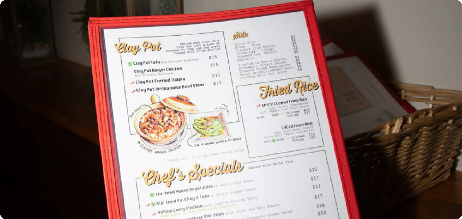 Close-up of a red-bordered restaurant menu on a table, showing sections for Clay Pot dishes, Fried Rice, and Chef’s Specials.