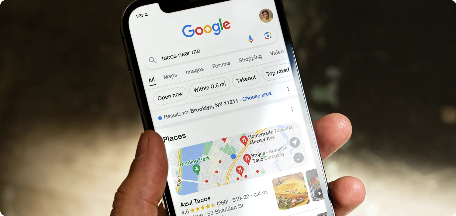 Hand holding a smartphone showing a Google search for ‘tacos near me,’ with map results and nearby restaurants displayed.