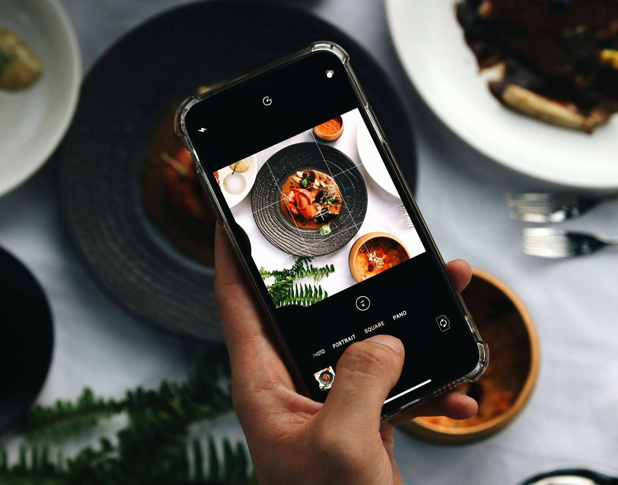 A hand snaps a food photo with a smartphone above a dining table