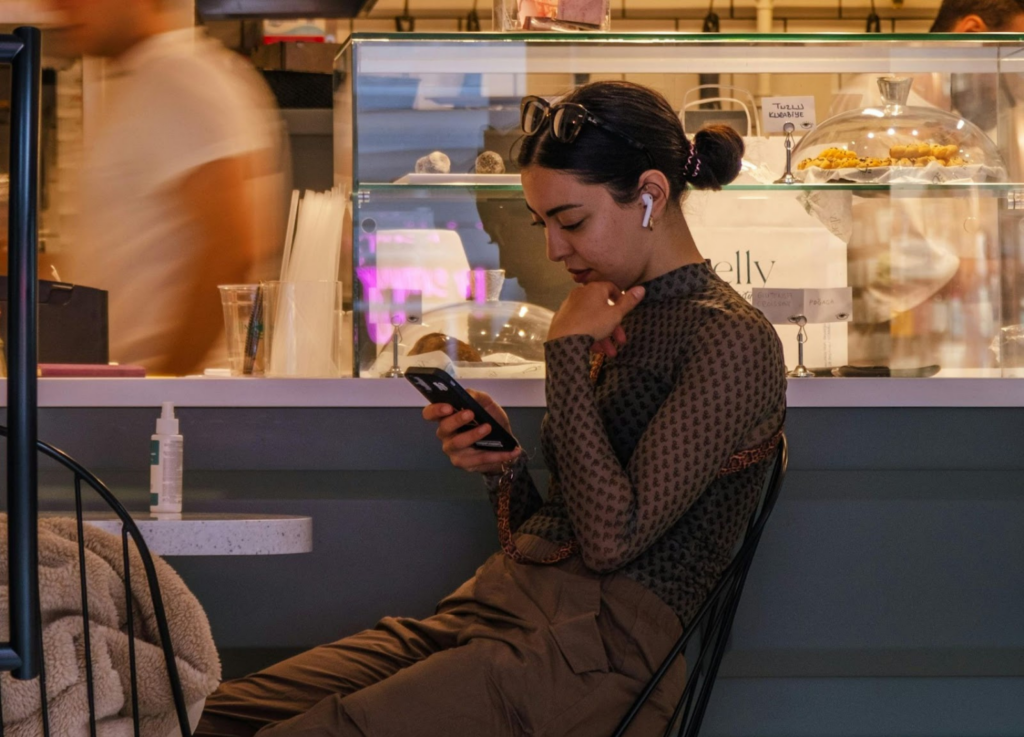 Woman holding and looking at a smartphone in a busy cafe