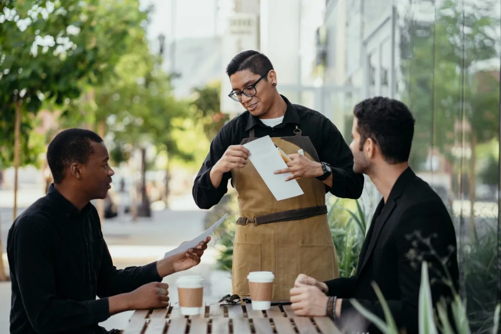photo of a smiling diner holding a menu while a server takes orders at a restaurant table with drinks.