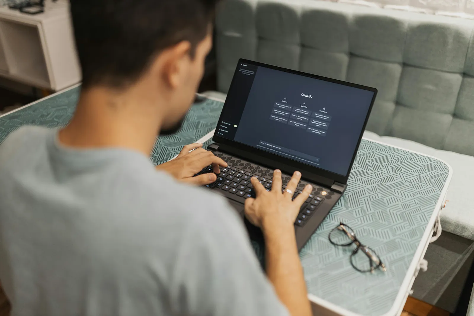A person using a laptop at a small table, with the ChatGPT interface open on the screen.