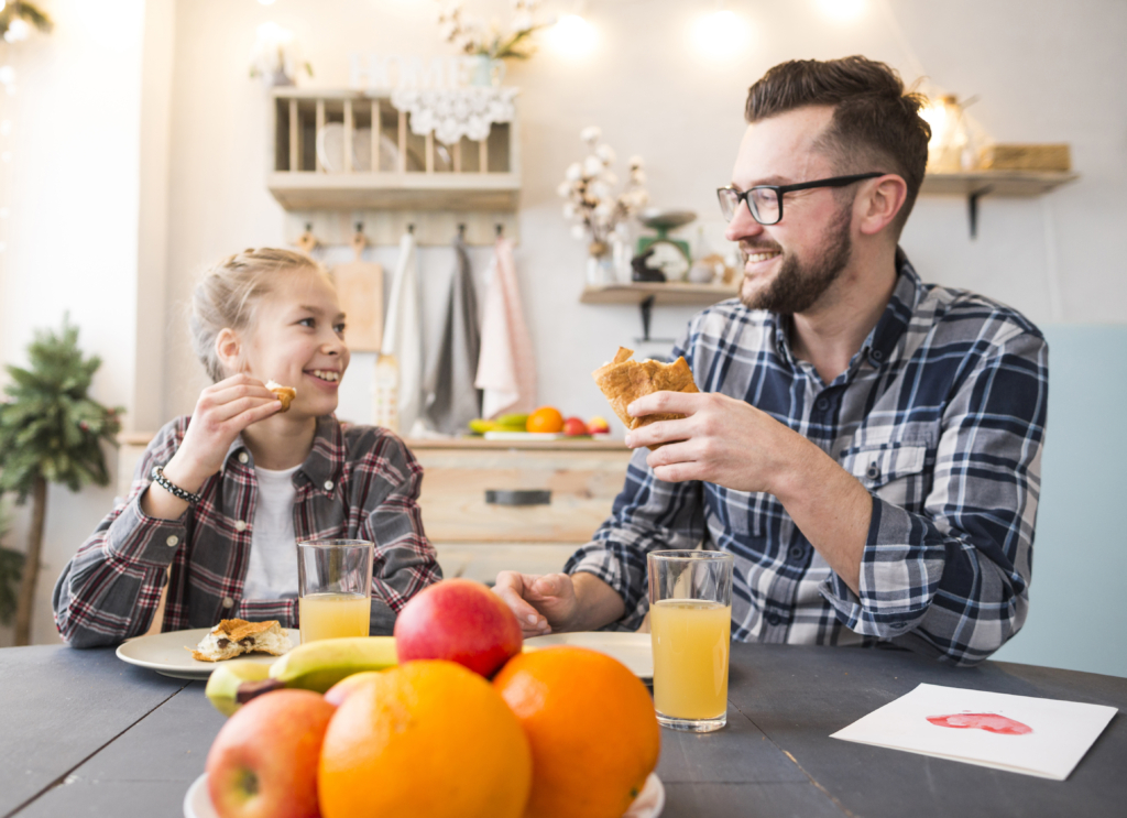 photo of a smiling father and daughter sharing breakfast at a cozy kitchen table with juice and fresh fruit.