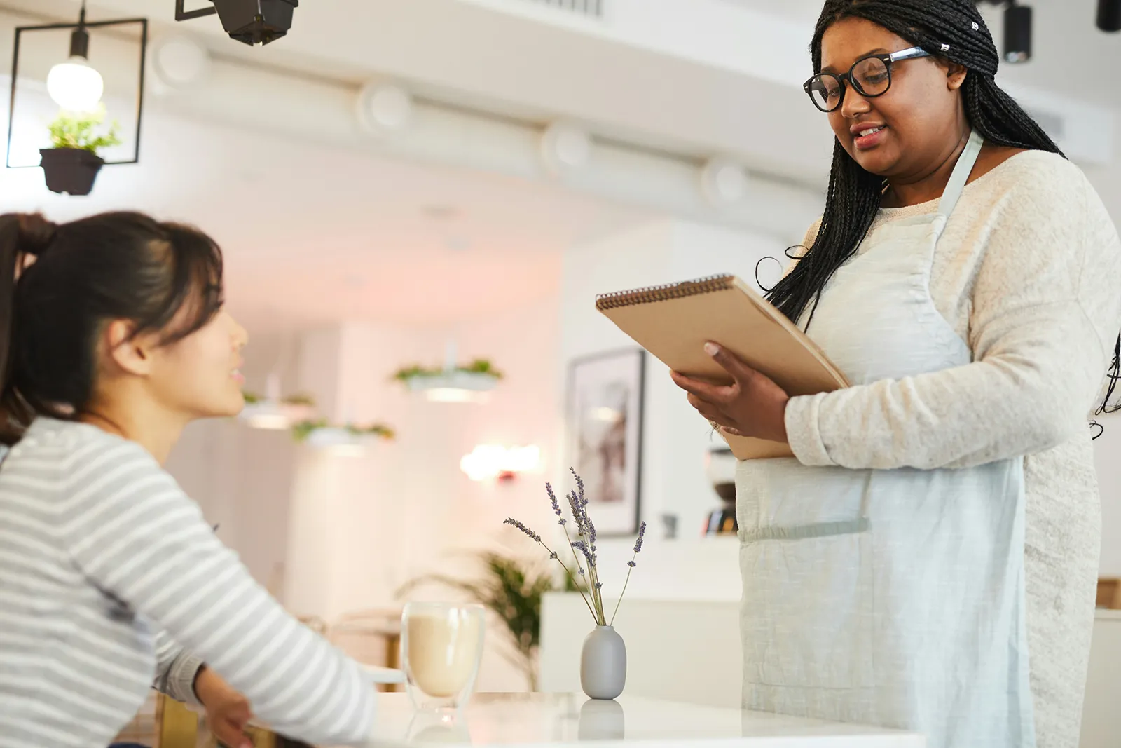 A café server taking an order from a seated customer, writing in a notepad.