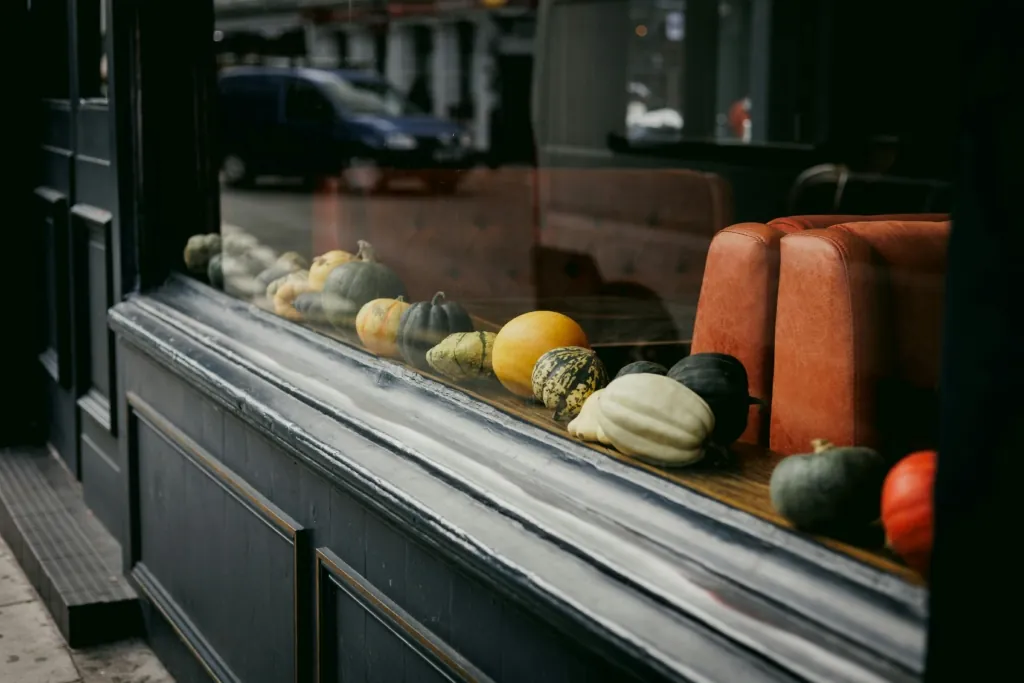 A photo of assorted gourds and pumpkins lined up in a restaurant window display with orange seating inside.