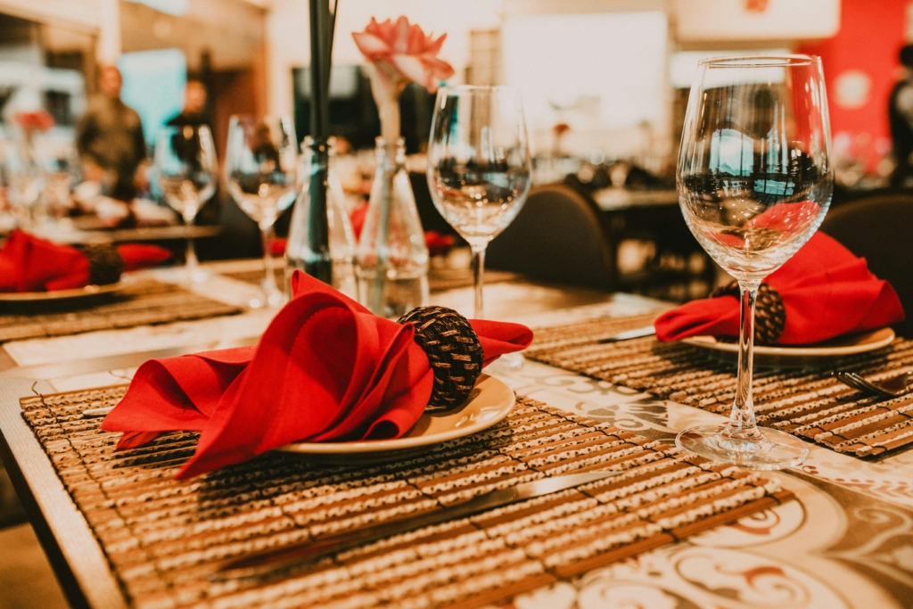 A photo of a holiday restaurant table setting with red napkins, wine glasses, and warm lighting creating a festive atmosphere.