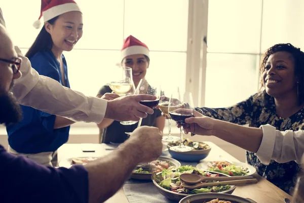 A photo of friends wearing Santa hats clinking wine glasses and smiling during a holiday meal at a restaurant.