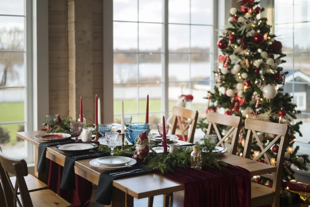 A photo of a beautifully decorated restaurant with a Christmas tree, wreath, and a table set for a festive holiday meal with candles and wine glasses.