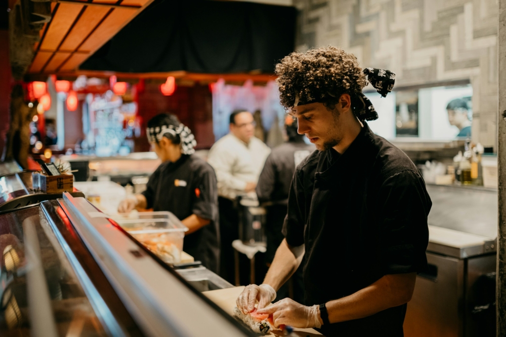 Chef preparing sushi behind the counter in a busy Japanese restaurant kitchen.