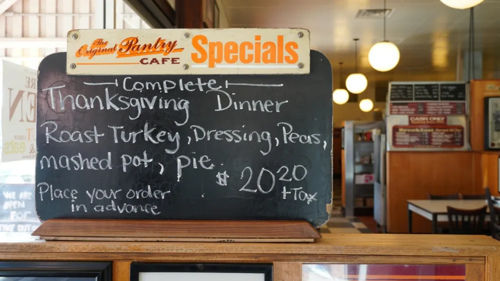 A handwritten chalkboard sign at a diner lists a Thanksgiving dinner special with roast turkey, dressing, peas, mashed potatoes, and pie.