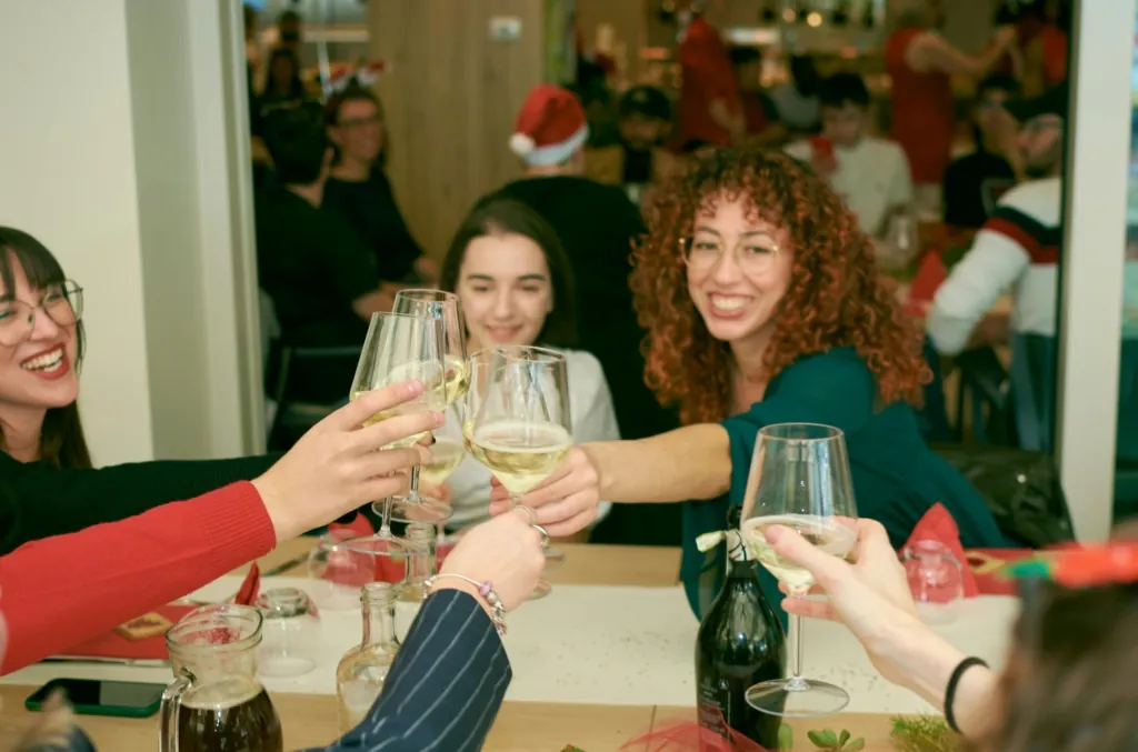 A group of friends raise glasses in a cheerful toast during a holiday dinner at a cozy restaurant.