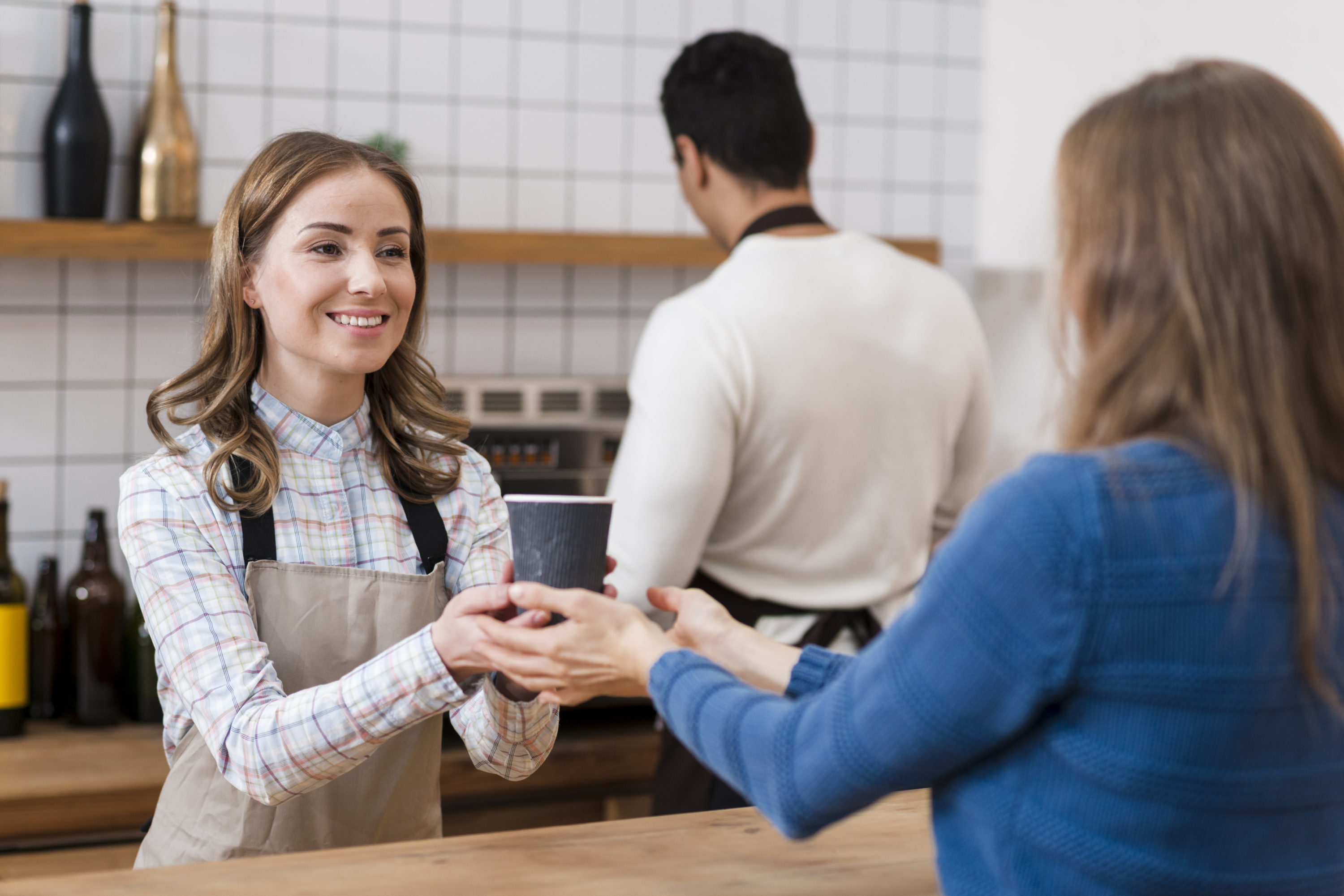 a photo of a barista smiling as she hands a takeaway coffee cup to a customer at the counter