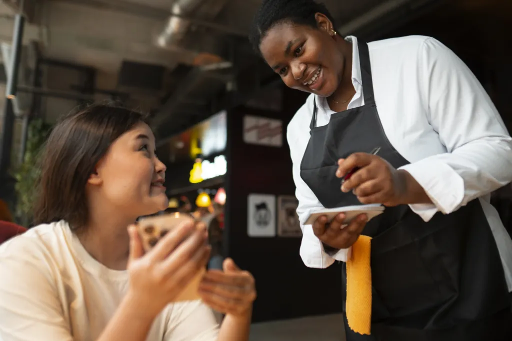 a photo of a smiling server at a restaurant while the guest looks up at her