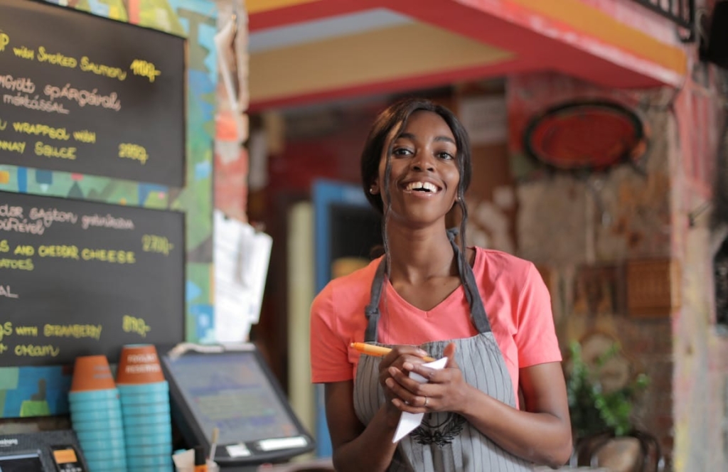 a photo of a restaurant server smiling behind the counter while holding an order pad