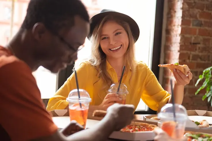a photo of diners enjoying pizza and drinks at a restaurant table with natural light in the background