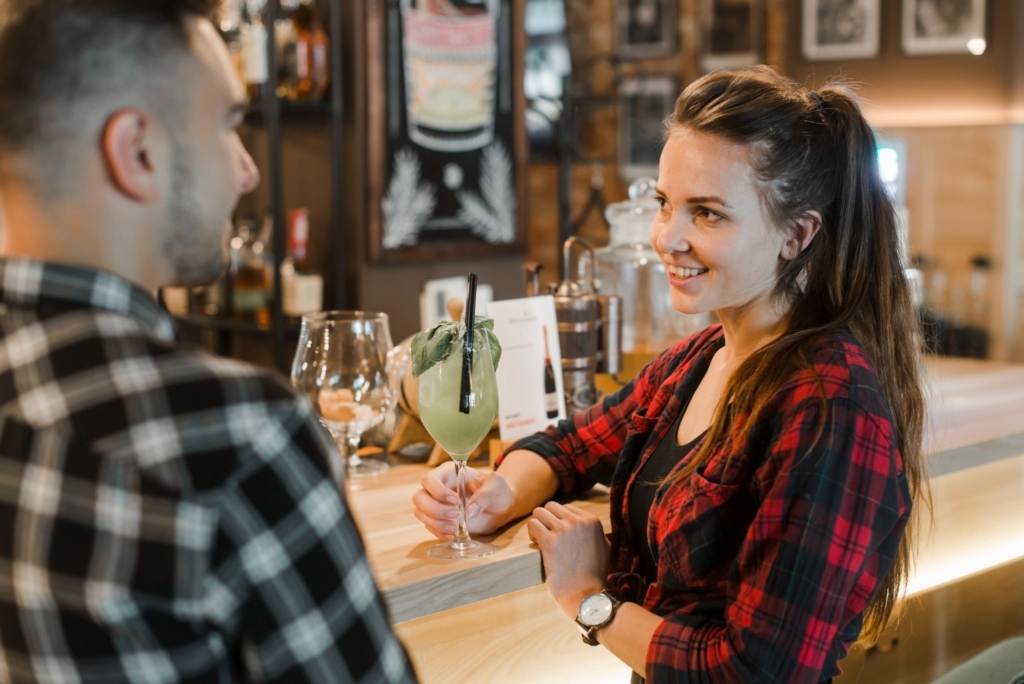 a photo of a bartender talking with a guest at the bar while holding a cocktail