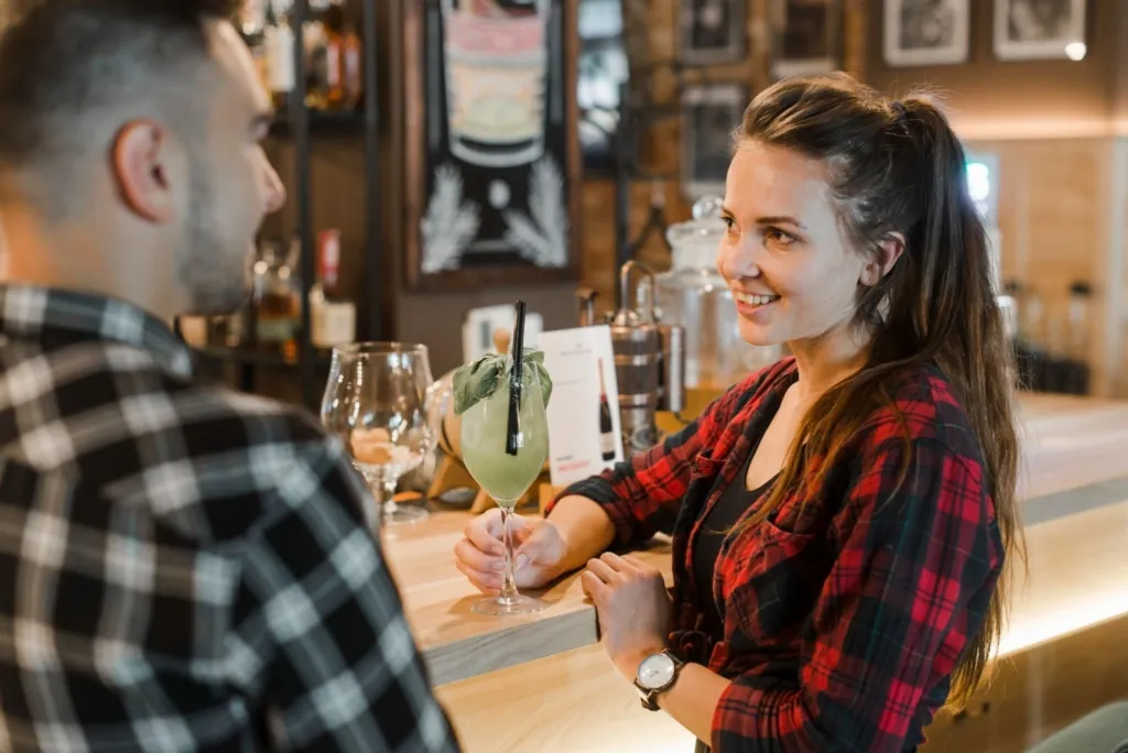 a photo of a bartender talking with a guest at the bar while holding a cocktail