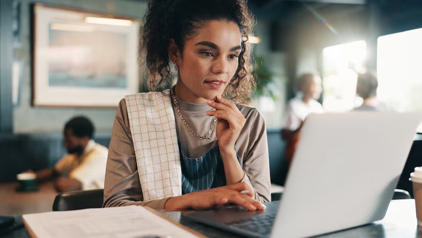 a photo of a restaurant owner wearing an apron, sitting at a laptop and reviewing information with a focused expression inside a cozy caf&eacute;.