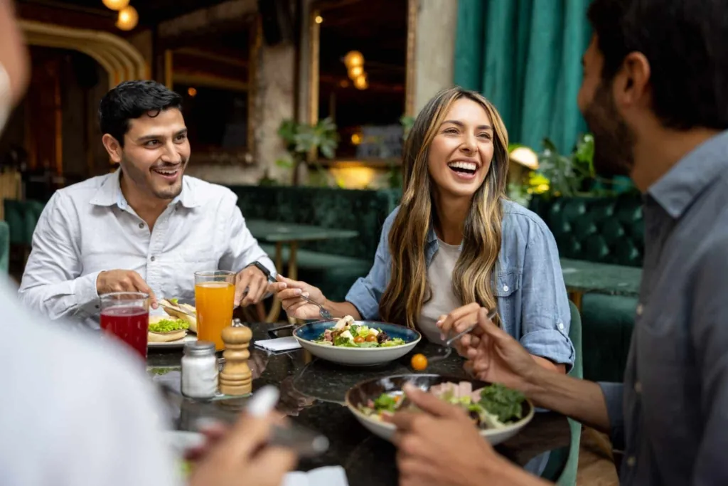 a photo of friends enjoying a meal and laughing together at a cozy restaurant table.