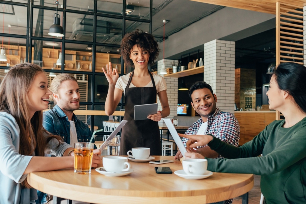 a photo of a server greeting diners with a tablet in hand as the group reviews menus at a caf&eacute;.