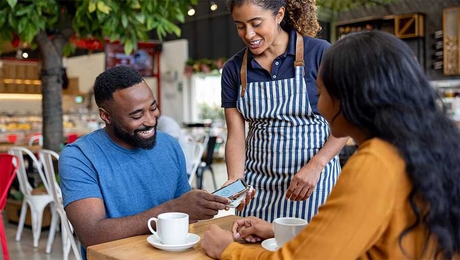 a photo of a server assisting two guests using a phone to place or review their order.