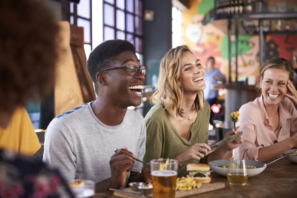 a photo of a group of diners laughing and enjoying food and drinks at a restaurant table, reflecting a positive customer experience and word of mouth dining moments.