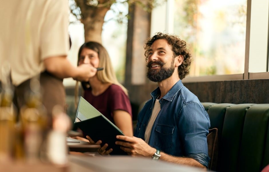 a photo of a server presenting a menu to seated guests at a restaurant table, highlighting in-person service and customer experience.