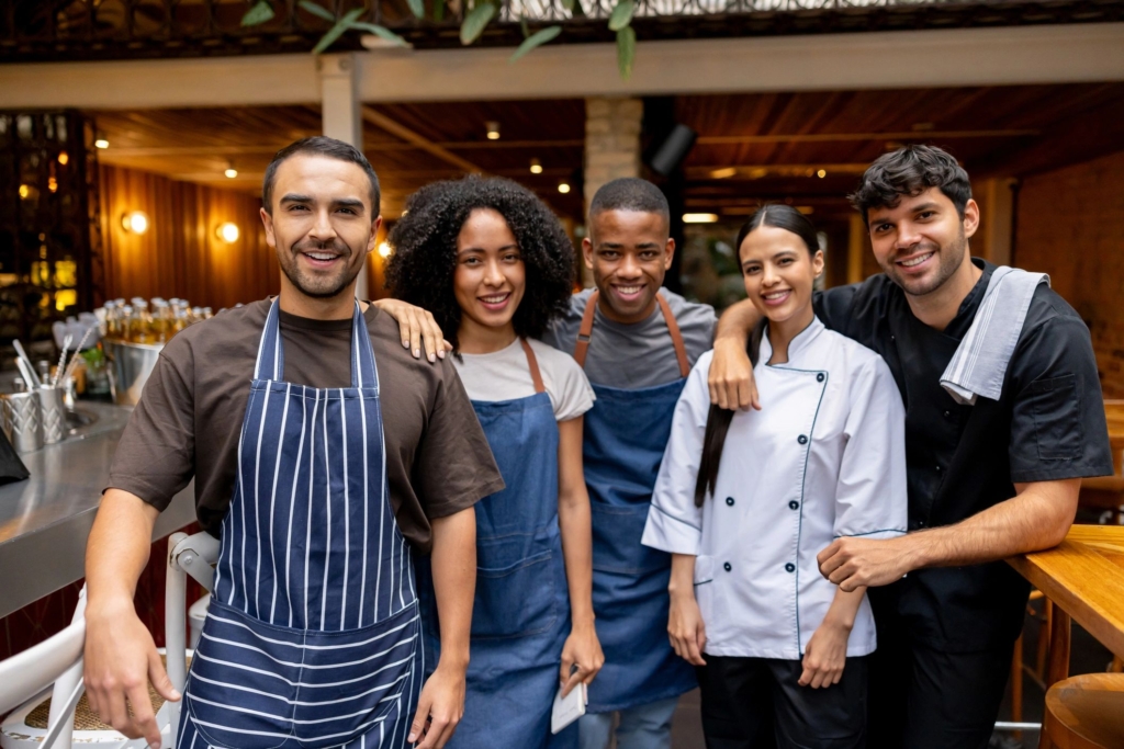 a photo of a restaurant team standing together in uniform, smiling at the camera, representing staff collaboration and day-to-day restaurant operations.