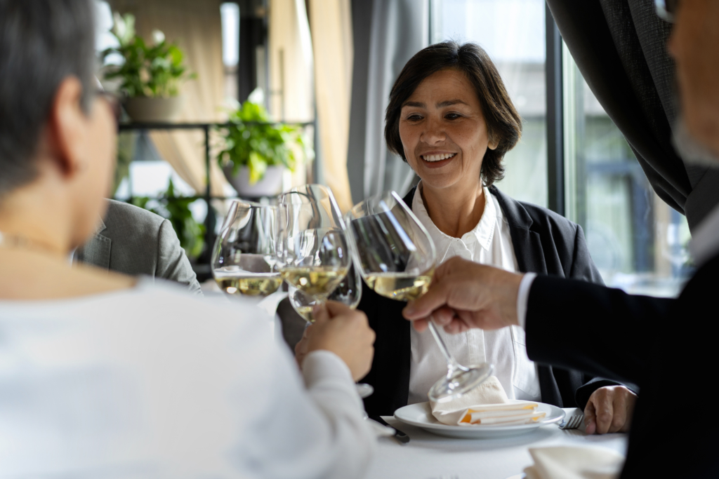 a photo of people raising glasses of white wine in a celebratory toast at a restaurant.