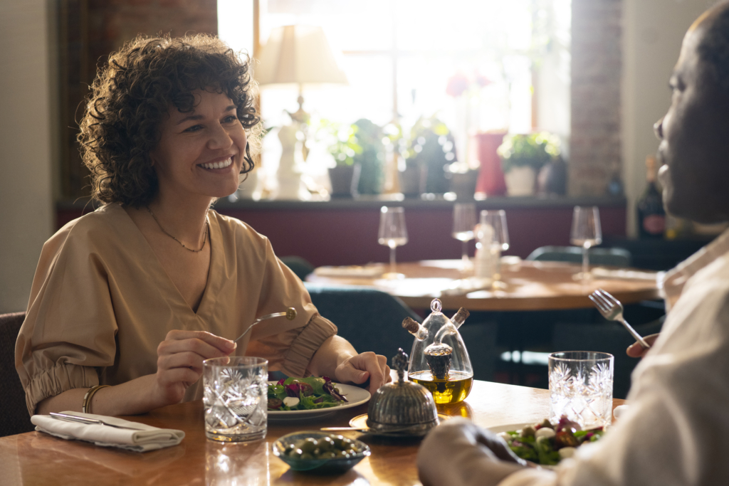 a photo of a woman smiling while eating a fresh salad in a warm, softly lit restaurant.