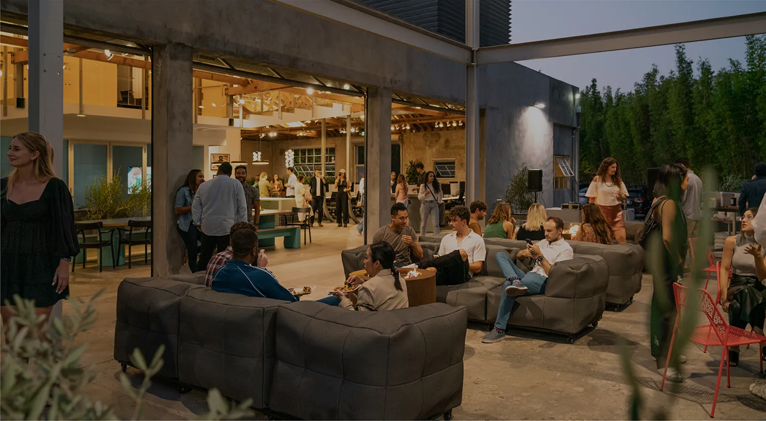 People socializing and dining in a modern open-air patio at ChowNow headquarters, with lounge seating, tables, and warm evening lighting.