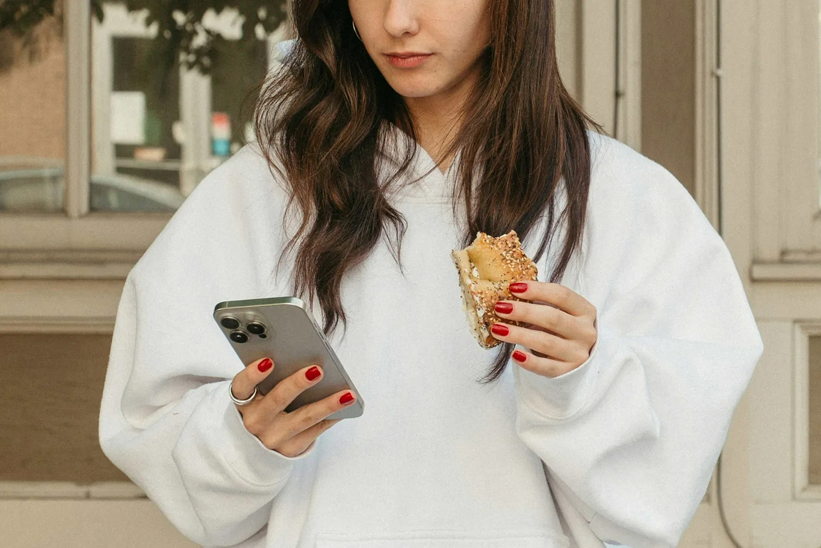 A woman checking her phone while holding a sandwich, likely ordering or reviewing food on the go.