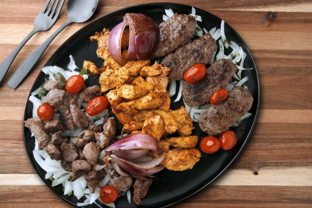 De Babel mix grill platter with lamb kofta, chicken tikka, beef cubes, roasted onions, and cherry tomatoes