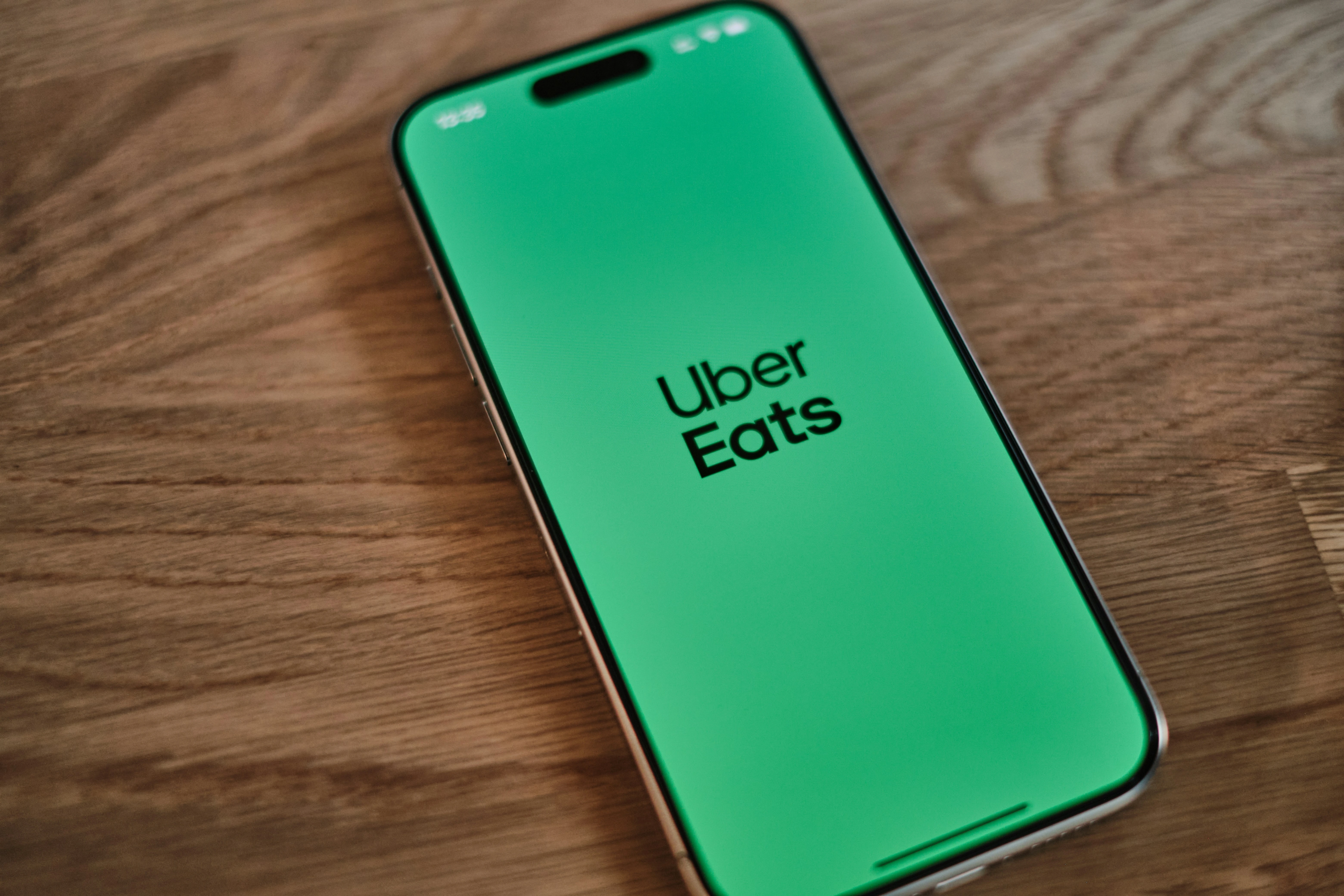 Uber Eats app splash screen displayed on a smartphone resting on a wood surface.