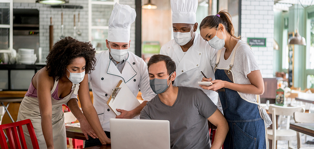 restaurant staff gathered together around a computer discuss tactics for restaurant success